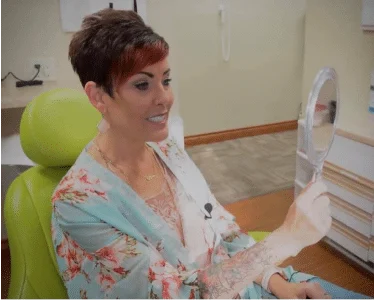 Julie grinning while looking to the mirror after dental work